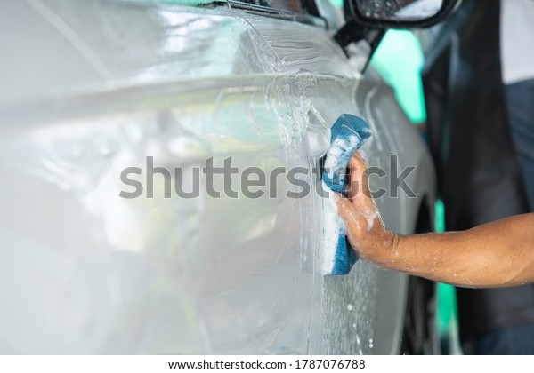 Adult labor using wet sponge\
with liquid soap washing a car close up with copy space, man wash a\
car.