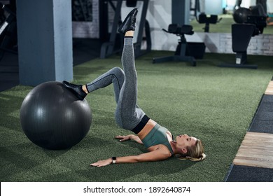 Adult lady lying on her back and putting one leg on a stability ball while stretching another in the air - Powered by Shutterstock