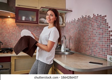 Adult lady in a white shirt and grey pants giving a wipe to a big plate with a dish-clout - Shutterstock ID 1864286437