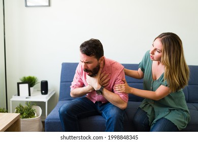 Adult Latin Man Choking With A Piece Of Food While Sitting On The Sofa With His Young Girlfriend At Home