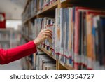 Adult Learning education concept. A woman is reaching for a book on a library shelf. The library is filled with books, and the woman is looking for a specific one