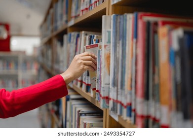 Adult Learning education concept. A woman is reaching for a book on a library shelf. The library is filled with books, and the woman is looking for a specific one