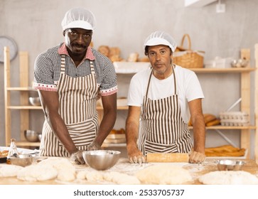 Adult male bakers shaping dough pieces and rolling out with rolling pin - Powered by Shutterstock