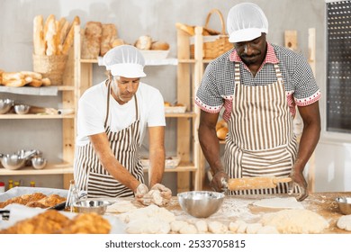 Adult male bakers shaping dough pieces and rolling out with rolling pin - Powered by Shutterstock