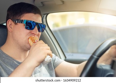 Adult Male Caucasian Person Eating Hot Dog Fast Food Snack While Driving Car On Sunny Day. Men Hsving Food While Driving Steering Wheel. Distracted Man In Vehicle. Bad Unhealthy Habit. Junk Food Go