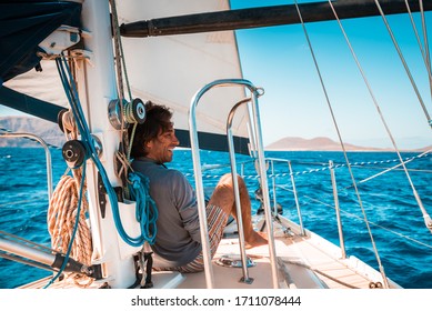 Adult male enjoying the view from the deck of a charter sail yacht with full sail on a sunny day with blue sky