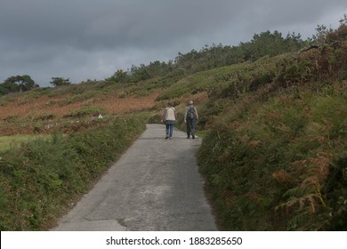 Adult Male and Female Walking Uphill Along a Concrete Coastal Path on the Island of Tresco in the Isles of Scilly, England, UK - Powered by Shutterstock