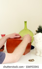 Adult Male Hands And Arms Holding Onto A Wood Urn Of Dear Departed Ashes Surrounded By Mementos On A White Fireplace Mantle.