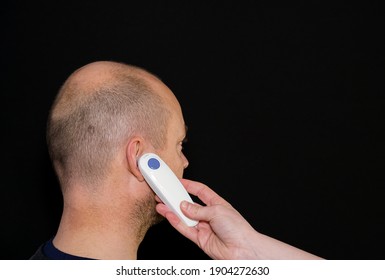 Adult Male Having His Temperature Taking With A Digital Ear Thermometer. Isolated On Black Background