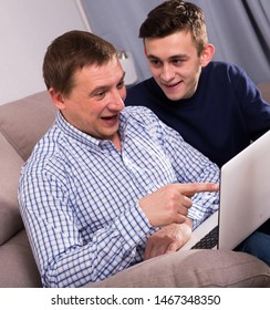 Adult Male With His Son Are Resting Together And Playing On Laptop At The Home.