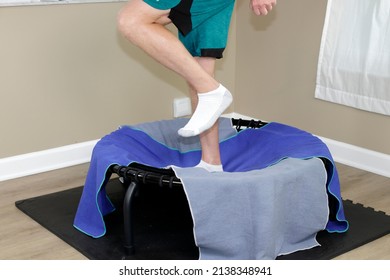 Adult male legs jogging on a round black rebounder covered with two workout towels. Left side view of legs of an adult white male exercising on a black round rebounder that has two workout towels.