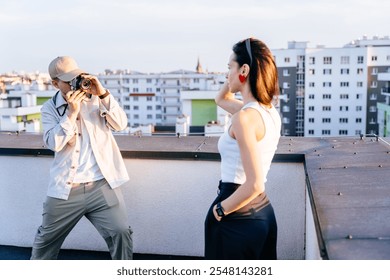 Adult male photographer capturing moment with female model on city rooftop. Casual, relaxed atmosphere with urban buildings creating artistic backdrop. Photographer passion amid urban landscape. - Powered by Shutterstock