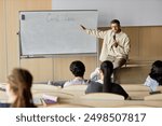 Adult male professor of law lecturing students while sitting on desk pointing at writing on whiteboard in university classroom, copy space