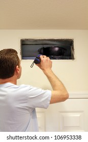 Adult male shining a flashlight into an air duct return vent to check for any need of cleaning dust or any other maintenance.
