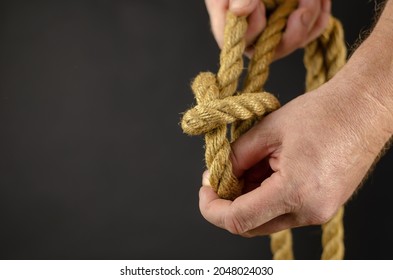 An Adult Male Is Spooling Rope Against Black Background. Hands Untie Knots On Yellow Burlap Rope. Close-up. Selective Focus.