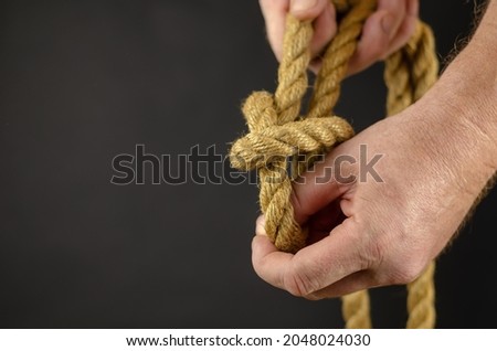 An adult male is spooling rope against black background. Hands untie knots on yellow burlap rope. Close-up. Selective Focus. 商業照片 © 