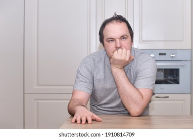 An Adult Man Of 40 Years Old In Casual Clothes Sits Thoughtfully At The Kitchen Table. Problems In Life With Despair, Grief, And Melancholy