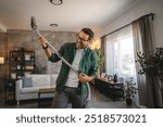 Adult man in an air guitar performance use a vacuum cleaner in a stylish and modern, natural light-filled living room setting