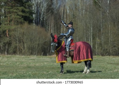 Adult Man In Ancient Knight Armor Rides Across The Field On A Horse In Armor In Red And Blue Blanket