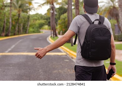 Adult man backpacker in cap standing by the road with thumb up, tourist hitchhiking, hailing taxi, traveling.