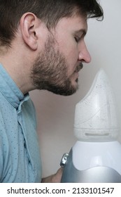 An adult man breathes steam, treats the airways with a nebulizer at home. The guy is sitting with an inhaler, a treatment for bronchitis, covid, a Nebulizer, a handsome man. Prevention and treatment