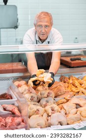 Adult man butcher in apron lays out raw chicken meat on counter in butcher shop - Shutterstock ID 2393282167