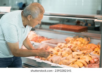 Adult man buyer in casual clothes chooses raw chicken meat in butcher shop - Shutterstock ID 2393282141