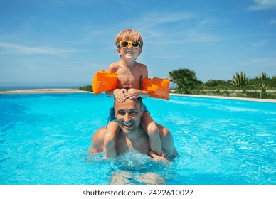 An adult man carries a boy on his shoulders while enjoying a swim in a pool, surrounded by a clear sky - Powered by Shutterstock