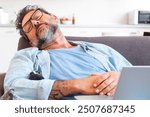 An adult man in casual attire taking a nap on the couch while working on his laptop, capturing a moment of exhaustion and relaxation. Reflects the challenges of freelance life and working from home