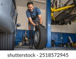 Adult man cheerful car mechanic in a blue shirt and gloves handles a tire confidently at an auto repair garage, showcasing professionalism and automotive expertise