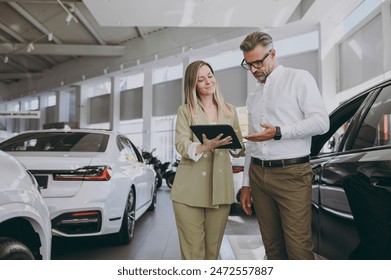 Adult man customer male buyer client wearing shirt consult with salesman signs documents choose auto want to buy new automobile in car showroom vehicle salon dealership store motor show. Sales concept - Powered by Shutterstock