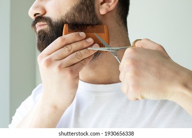 Adult Man Cutting His Own Beard And Mustache With Scissors And Comb. Bearded Male Trimming Hair On Face At Home. Do It Yourself Self-made Haircut.Selfcare During Quarantine Isolation