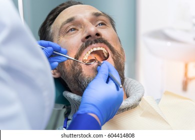 Adult man at the dentist. Doctor checking teeth. Precise dental diagnosis.