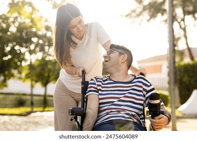 An adult man with a disability sits in an automatic wheelchair with a young woman in a park at sunset.The woman and the man look at each other happily. Concept of support for disabled people.