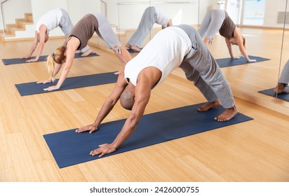 Adult man doing yoga with group of people in fitness studio, standing in stretching asana Adho Mukha Shvanasana known as Downward Dog pose.. - Powered by Shutterstock