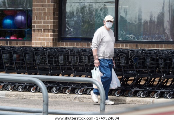 Adult man\
with a face mask during the Covid19 pandemic, carrying plastic bags\
after shopping at a local grocery\
store
