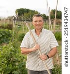 Adult man farmer with rake standing at farm outdoor