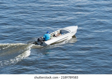 Adult man fast moving in white motorboat on the river. He drives the motor and looks for fish. Waves on the water and foam after speed. Water transport. Top view. Lifestyles. - Powered by Shutterstock