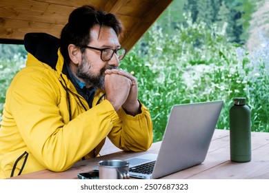 Adult man freelancer traveler wearing yellow jacket anywhere working online using laptop and enjoying nature park mountain around. Modern traveler entrepreneur business lifestyle. Traveling computer - Powered by Shutterstock