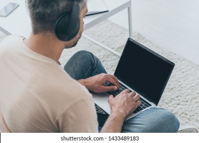 adult man in headphones sitting on floor and using laptop with blank screen