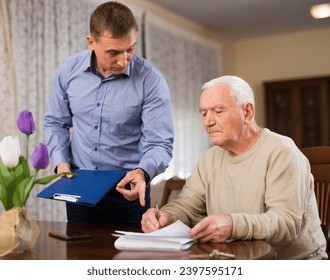 Adult man helping his senior father filling out financial documents at home - Powered by Shutterstock