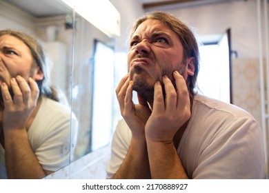 Adult Man With An Itchy Beard In Front Of A Bathroom Mirror