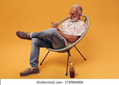 Adult man in jeans and stylish shirt chatting on phone. Gray-haired guy with beard and in tattoos holds smartphone on isolated background - Powered by Shutterstock