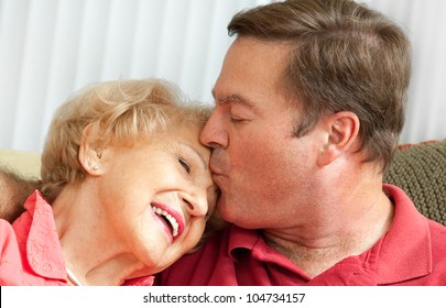 Adult man kissing his elderly mother on the forehead.  Closeup portrait.