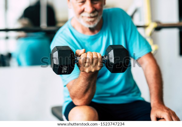 adult\
man and mature senior at the gym working his body with dumbbell -\
one man hapy training indoors sitted on the\
bench