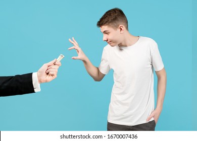 An Adult Man Offers The Teenager Money And The Guy Agrees. Hand Of A Business Man In A Jacket Holds Out Rolled Up Dollars. Teen Reaches For Them