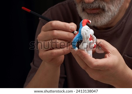 An adult man paints a clay toy after firing. A clay toy is pre-primed with whitewash.                               