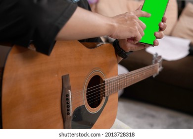 Adult Man Play Guitar Searching For The Chord And Note Sheet. Guitarist Learning How To Play Song. Technology Of Smart Phone And Musician.