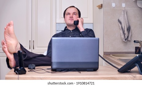 Adult Man Put His Feet On The Table While Talking On The Phone From Home Office, Humor. Problems With Remote Work From Home During Lockdown