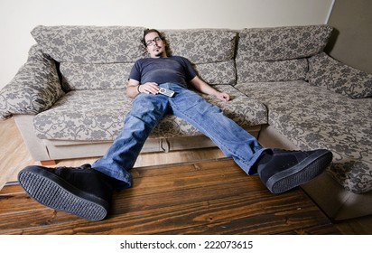 Adult man resting in sofa like a couch potato with remote control on belly